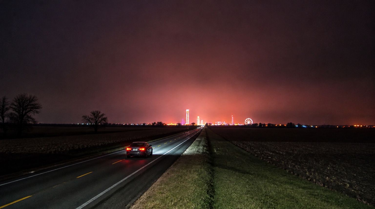 Dark sedan on a two-lane Oklahoma highway at night heading toward the glow of a casino complex