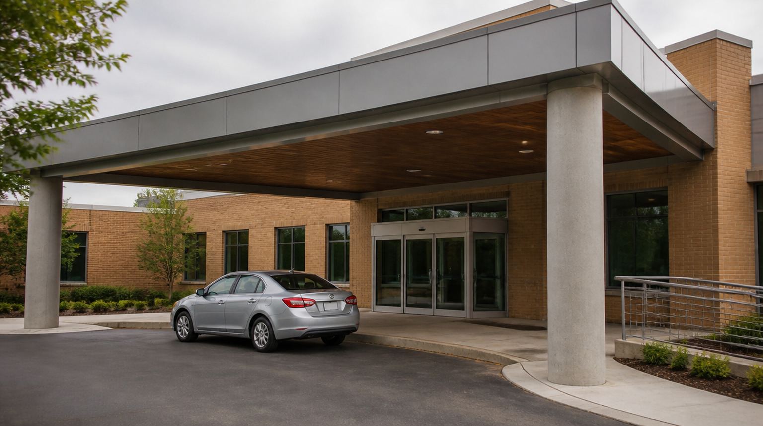 Covered patient drop-off entrance at a small-city medical clinic with a wheelchair ramp and a waiting sedan